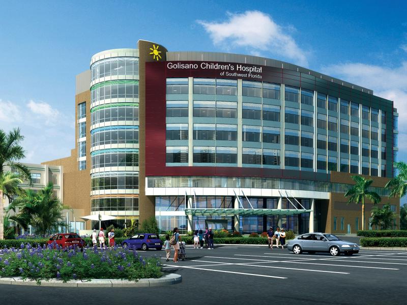 Exterior of hospital, rounded building with large glass windows and parking lot in front.