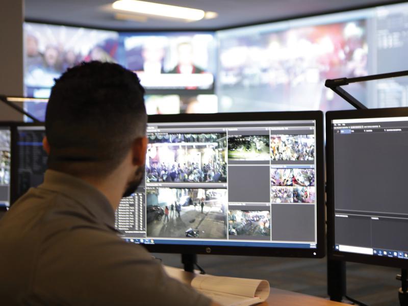 Man viewed form behind, in front of monitoring computer screens.