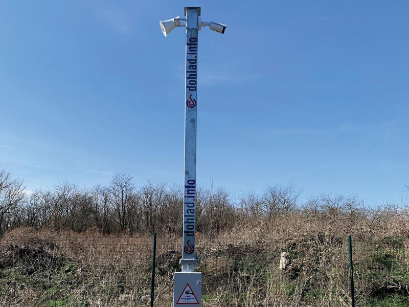 Axis camera and hornspeaker on pole, brown grass in background.