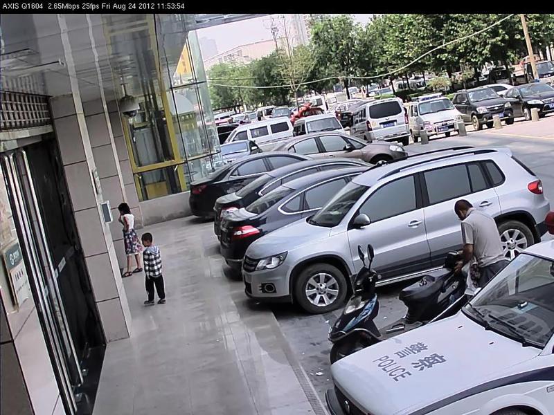 Parking lot in china, cars viewed from their left angle, two people on sidewalk.