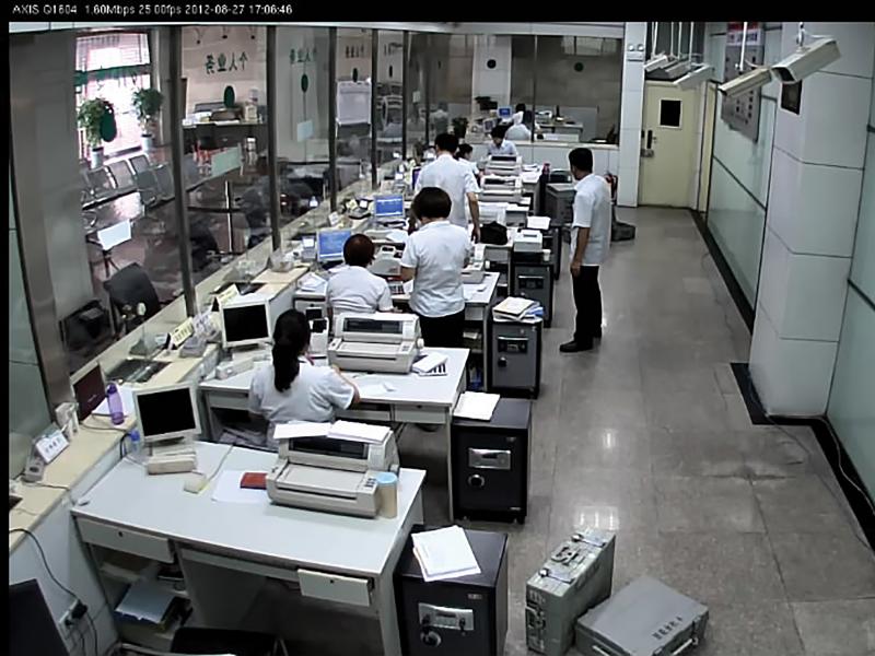 Bank office in China, people sitting at their desk viewed from behind, one standing.