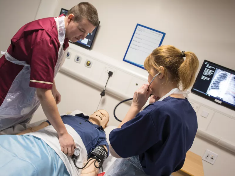 One man and one women at clinic standing over practice doll.