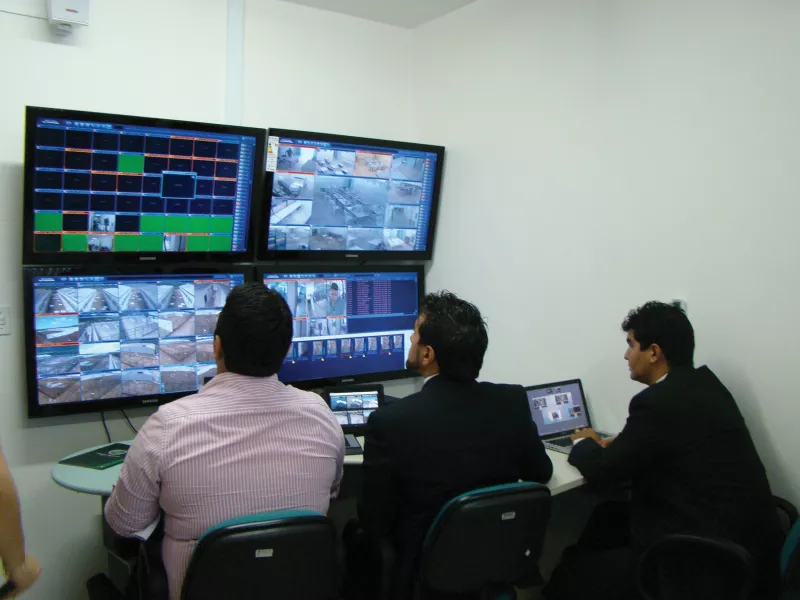 Three men viewing monitor screens of prison.