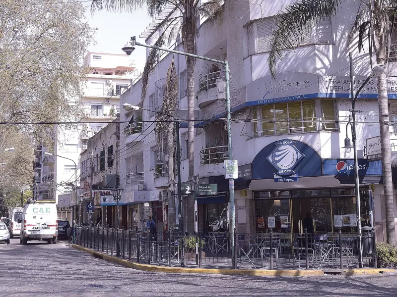 Street corner of light building with blue entrance on corner, palm trees in front.