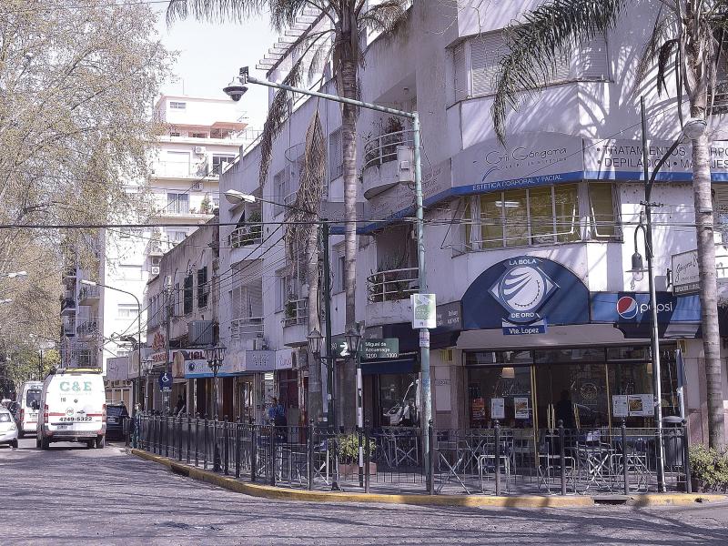 Street corner of light building with blue entrance on corner, palm trees in front.