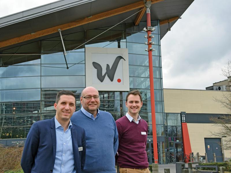 Three men in front of glass building with black W on it.