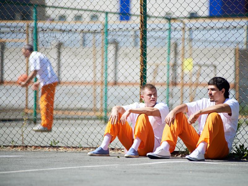 2 prisoners sitting outside along fence