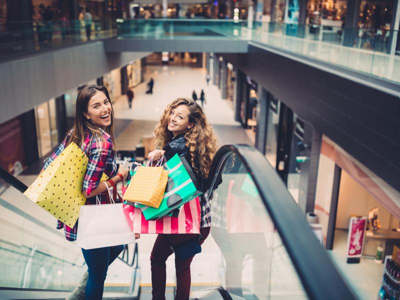 Two women stands in a escalator smiling with several shoppingbags