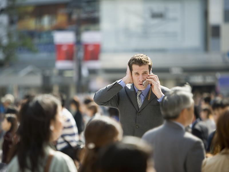 Busy city crowd one man in focus trying to talk in his phone but the surroundings is too loud