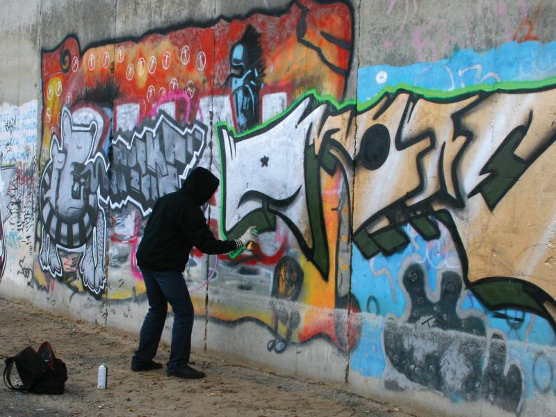 Graffiti man vandalize by spray printing a public wall