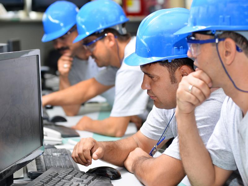 A group of men with blue working helmet looking at a computer screen