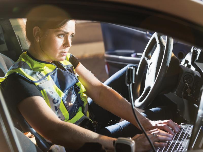 Police woman sits in her car writing on a keyboard in a car