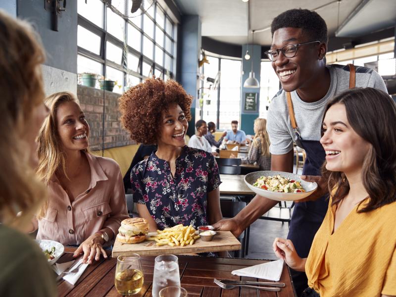 Happy waiter serving food for four womens