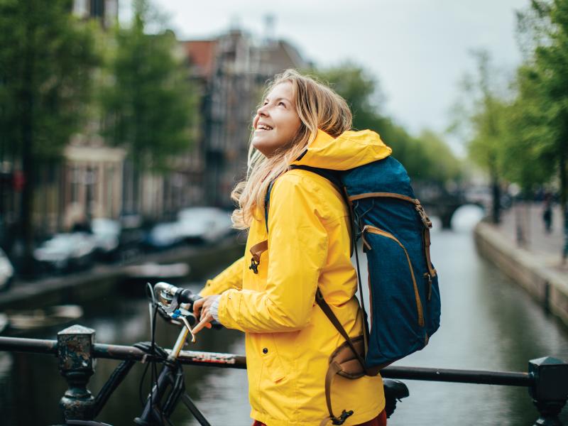 Woman standing with a yellow rain coat on her bicycle in front of a canal smiling