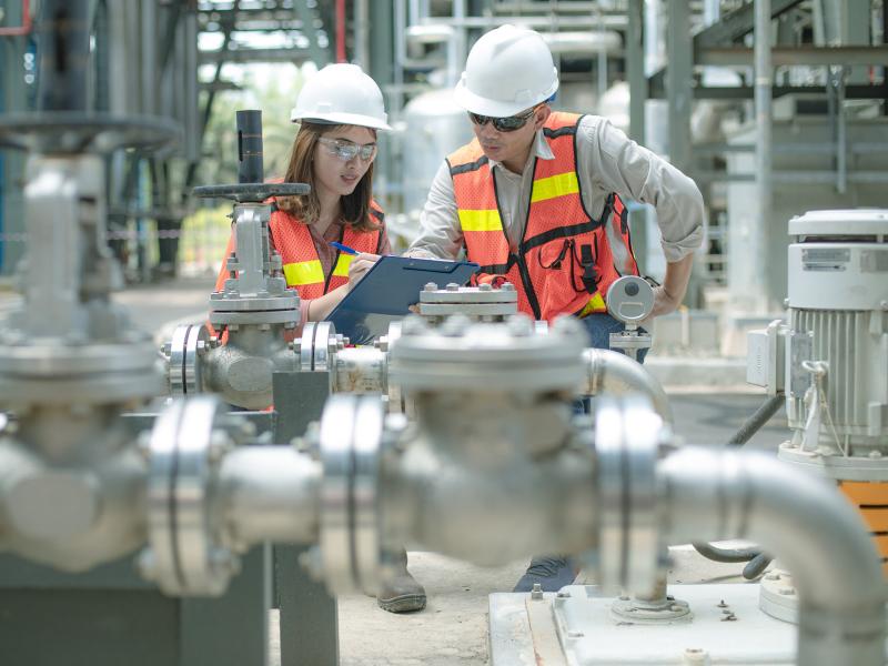 Industrial workers, woman and man, in an industry workshop with hardhats and safety vest