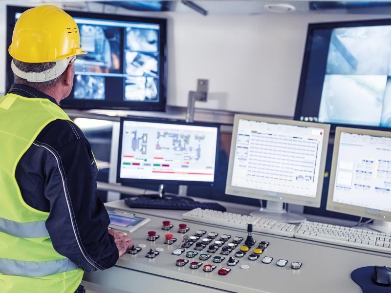 Control room with c´screens and a worker with yellow working helmet and safety vest