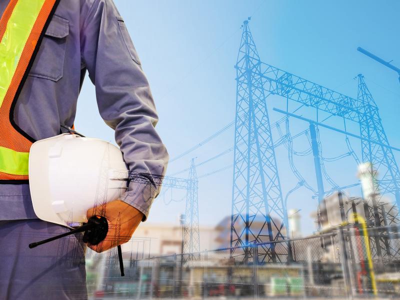 Worker holding a hardhelmet in an outdoor enviroment infront of electrial station