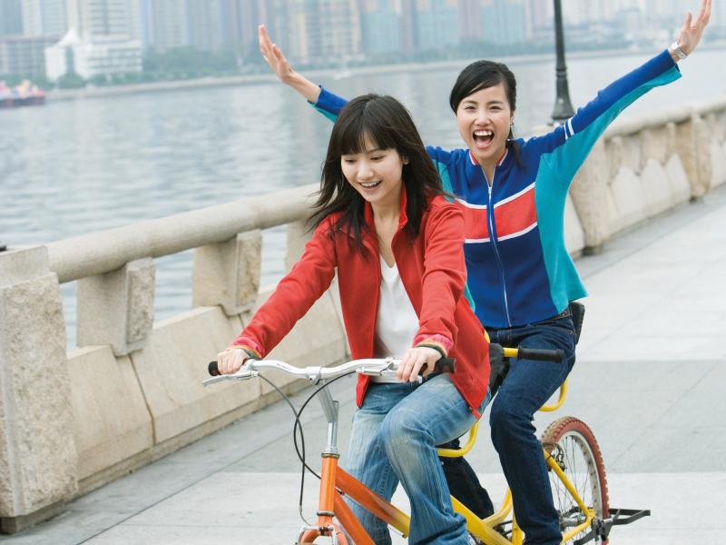 Two young women cycling a tandem bicycle.