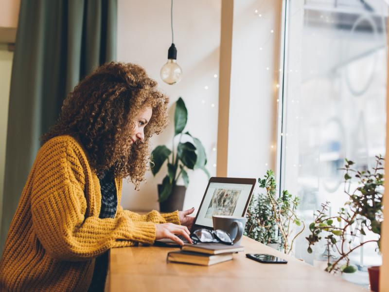 woman in yellow sweater works at her laptop