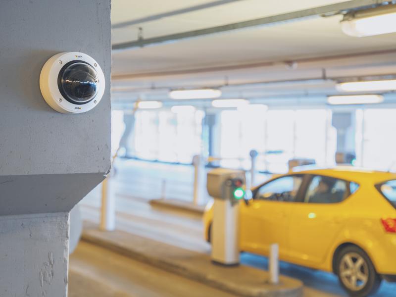  AXIS P3245-LVE-3 License Plate Verifier Kit, mounted on a wall in a carpark entrance. Yellow car in the background. 