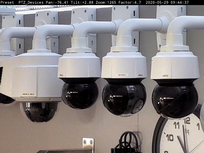 Seven cameras in the color white and black positioned on a wall above a clock