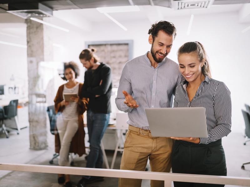 Man and woman are standing and looking at a laptop