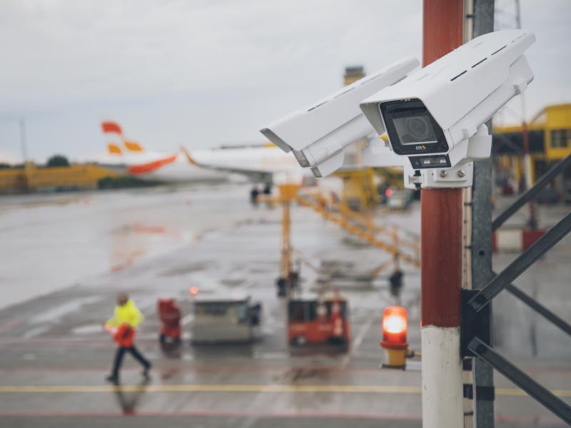 Корпусная камера AXIS Q1656, установленная на столбе на открытом воздухе, на заднем плане - самолет.