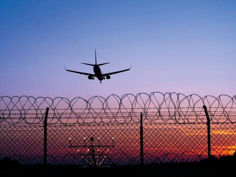 Airplane landing in sunset behind fence