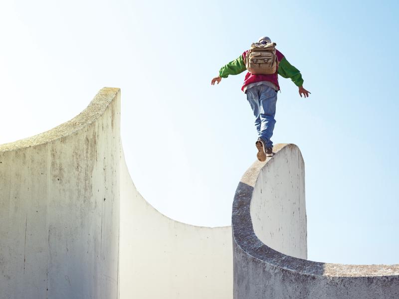 A backpacker balancing on a curved wall with blue skies in the background