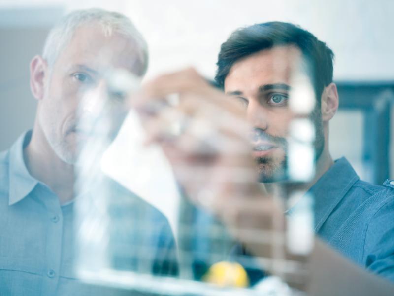 2 men writing glass wall