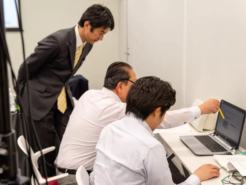 Three men looking at a screen.
