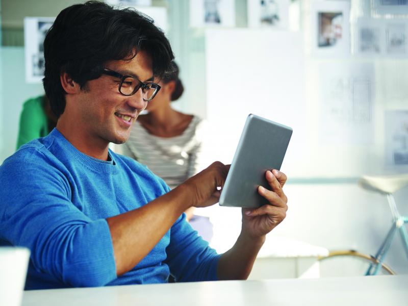 Man with glasses smiling looking at an ipad