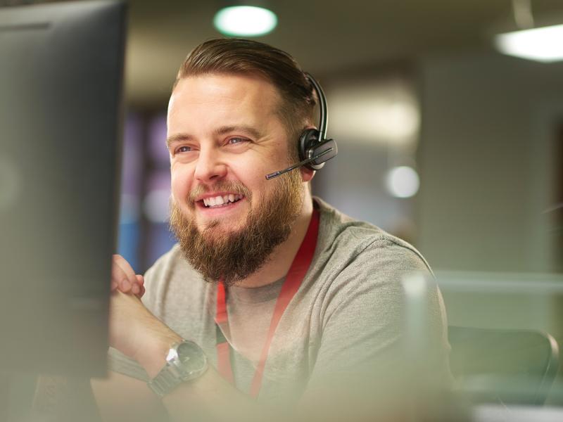 a man wearing a headset, smiling, sitting in front of a computer screen