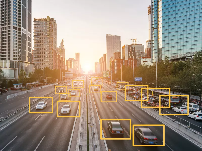 cars driving on a road in a big city, big buildings in the background