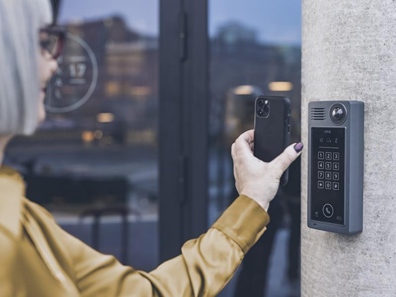 Person with short hair and wearing a yellow jacket is using qr code on their phone in front a reader