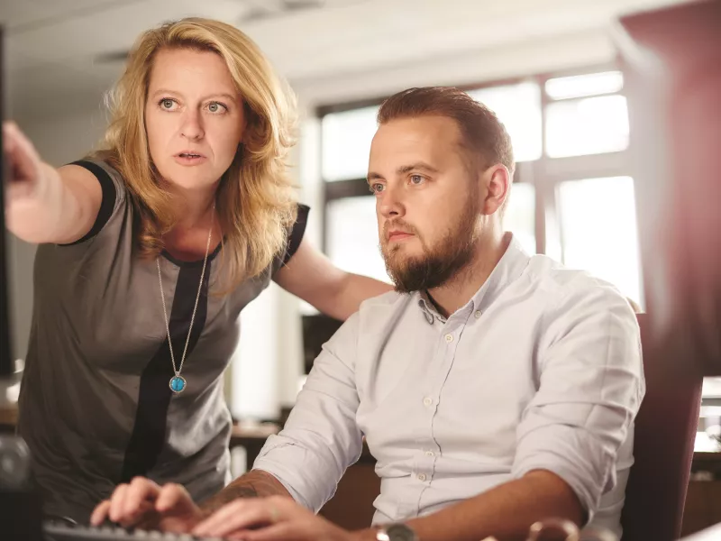 a man and a women in an office environment, looking at a computer screen