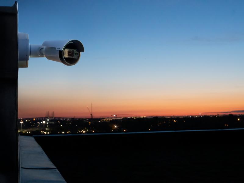 P1467-LE mounted on a building. Background is a city skyline in dusk.