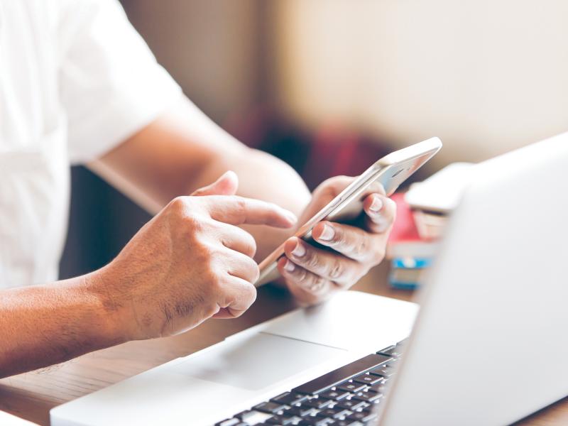 Hands holding a smartphone by a laptop.
