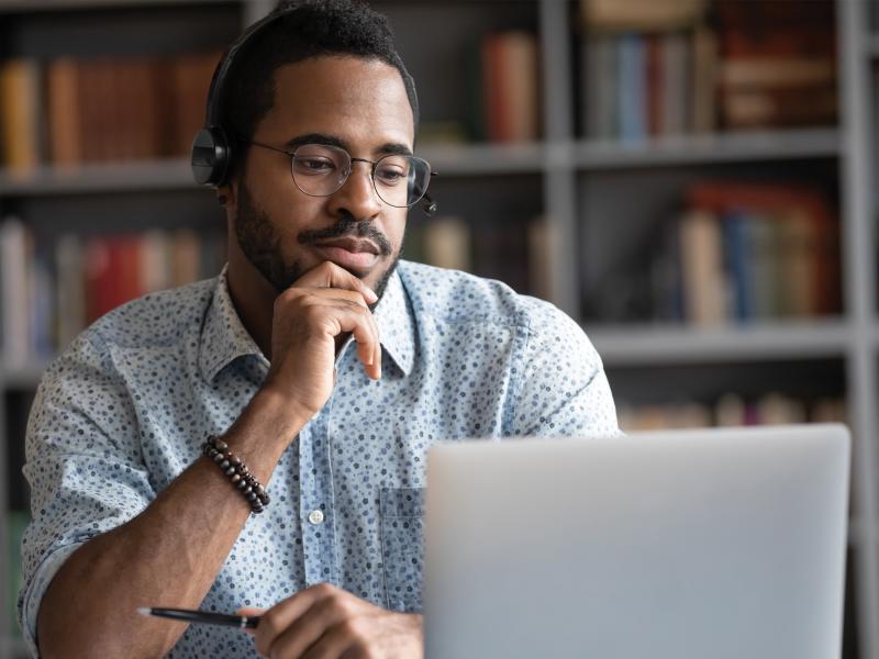 Man in glasses by laptop, wearing headphones. 