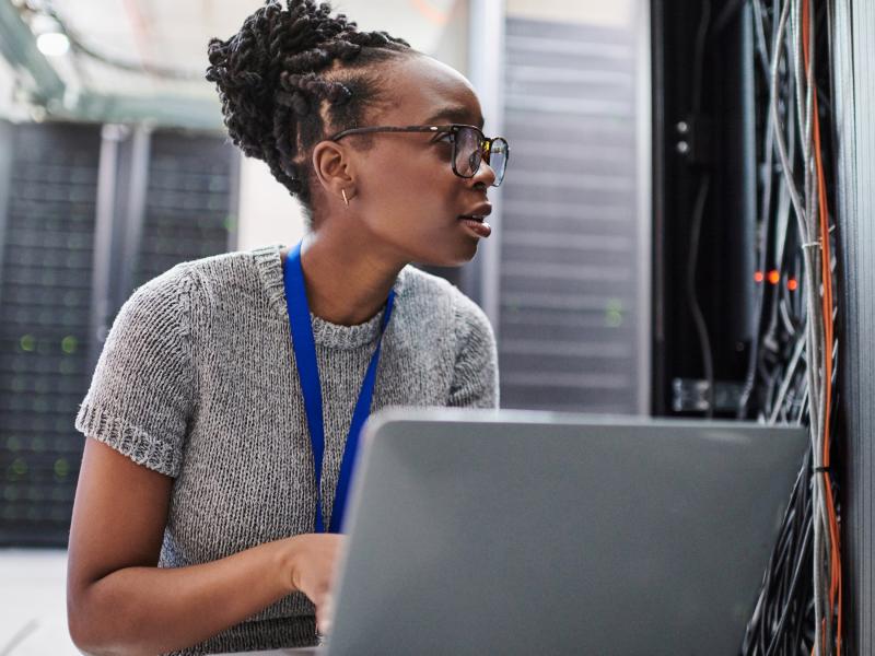 young woman sitting in front of a laptop in a server room