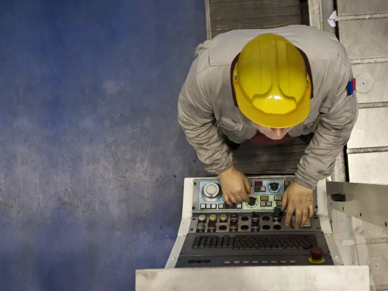 Factory worker with yellow hat, working on machine.