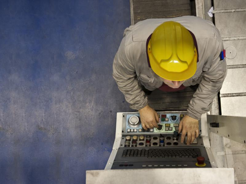Factory worker with yellow hat, working on machine.
