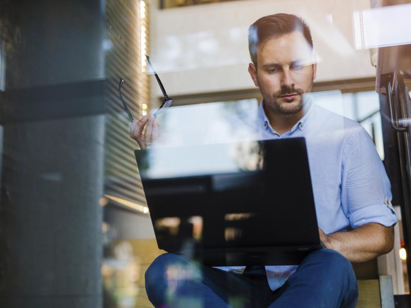Business man sitting on stairs with a laptop in his knee.