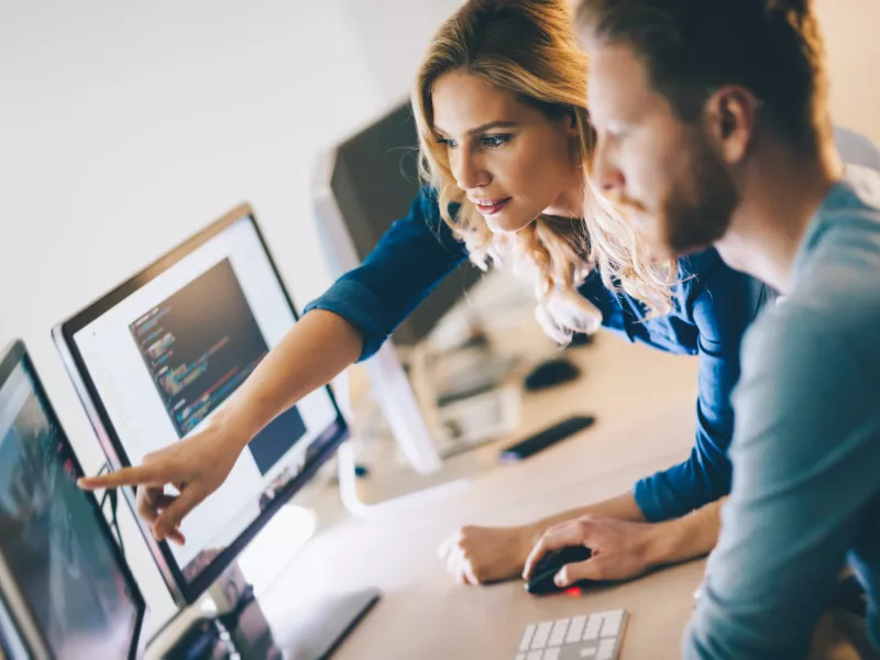 Two people in front of a computer screen, one of them pointing at it.