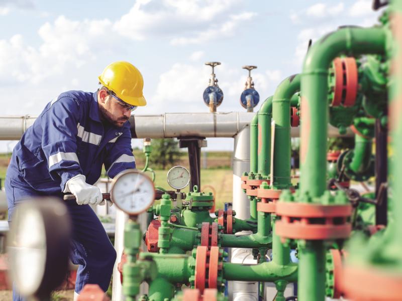 worker wearing a hardhat, adjusting the oil pipes at a refinery