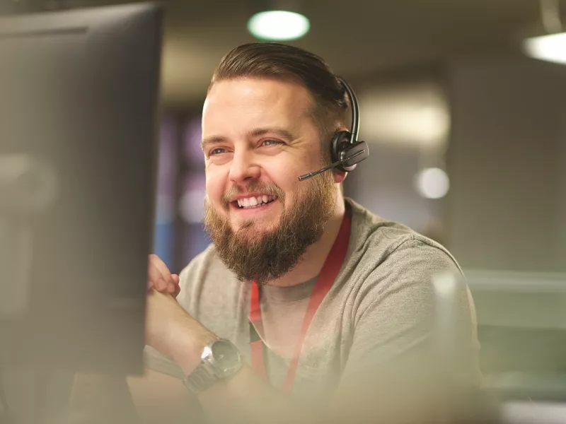 man who is  sitting in front of a computer screen, wearing a headset, smiling
