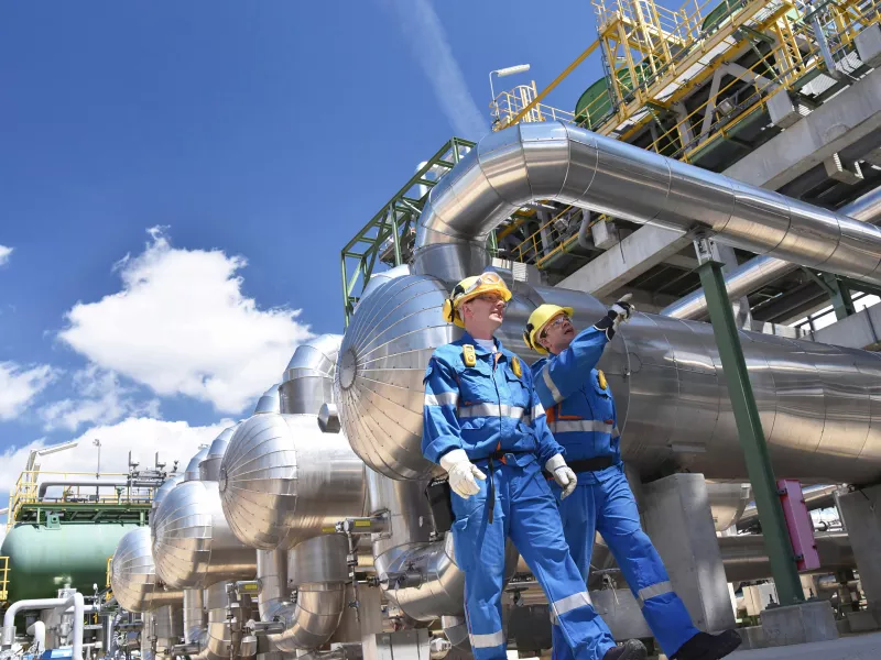 Two men wearing hard hats in an oil refinery