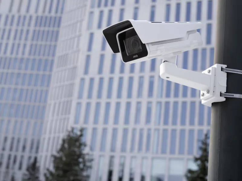 Camera on pole outside with large building with lots of windows in background