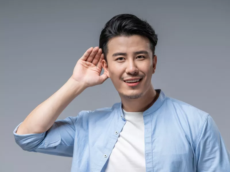 Happy young man holding his hand close to his ear