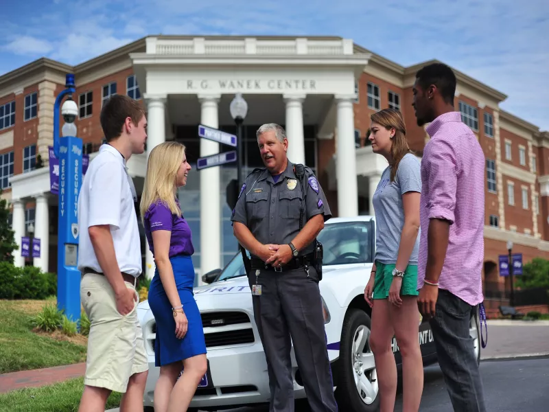 Security officer talking with students in front of academic building at High Point University
